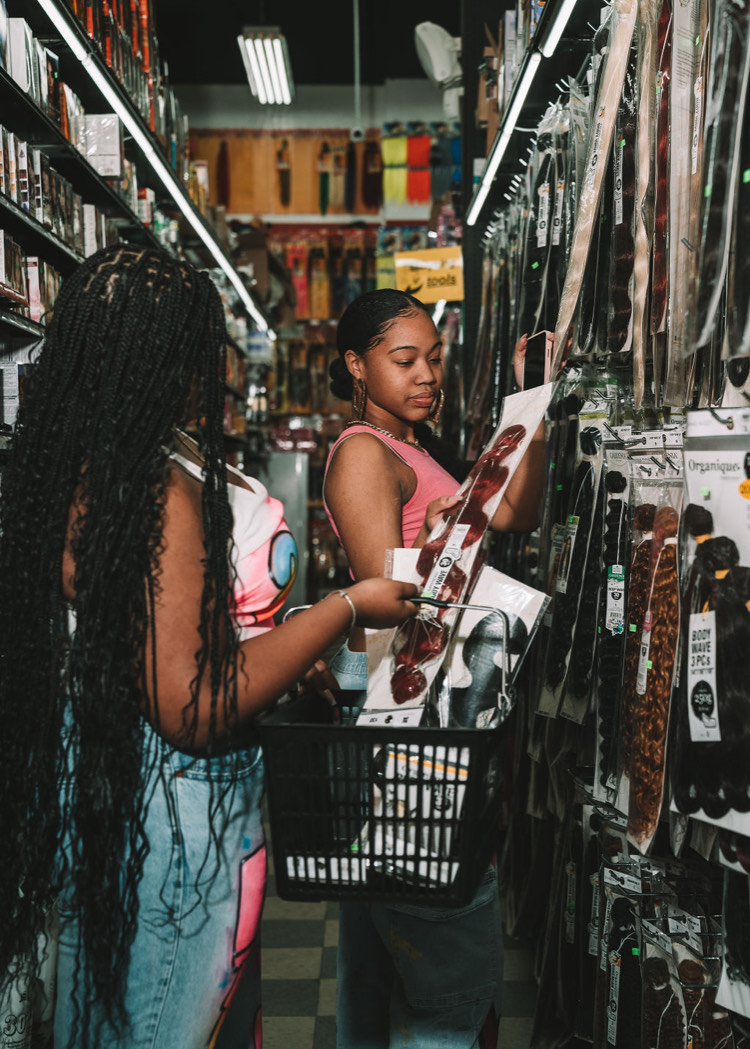 Two models browse an aisle full of weaves at their local beauty supply store. 