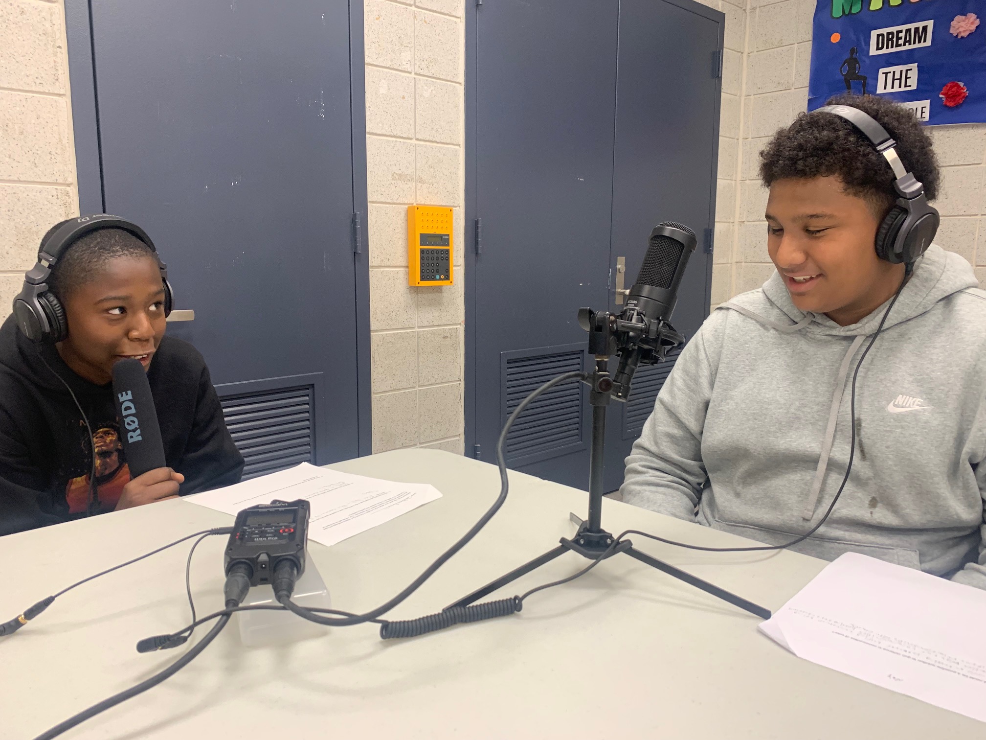 Two students smiling with headphones and microphones. 