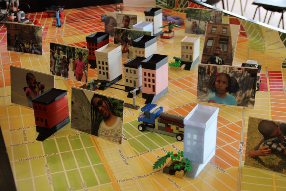 A photograph of the Gentrification Through the Eyes of Youth multimedia display that includes a street map, model buildings, Lego structures, and pictures of students in their community. 