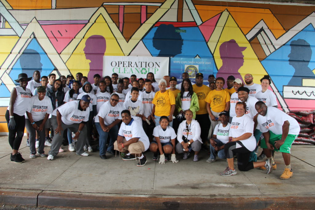 A large group of Laurelton residents gathered in front of a colorful mural and an Operation Clean Up sign. 