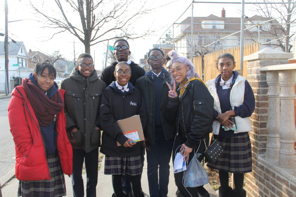 A group of seven students dressed in school uniforms and winter coats One holds a clipboard used to collect signatures from local residents. 